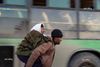 En syrisk mand bærer en ældre kvinde ud af det østlige Aleppo. I baggrunden ses en af de grønne busser, som har fragtet civile og oprørere ud af byen. Foto: Thiqa News via AP