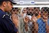 En græsk politimand taler med illegale indvandrere bag et af de høje hegn, der omgiver modtagelsescentret i Komotini i det nordlige Grækenland. Der var sidste år optræk til optøjer i centret, der ligger 820 km nord for den græske hovedstad, Athen. Foto: Nikolas Giakoumidis/AP