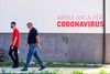 People wearing face masks walk in front of Coronavirus Ambulance in Pristina, on August 29, 2020. - Inside Kosovo's hospitals, beds are filling up with the sick and the dying as Covid-19 tears through one of Europe's poorest corners. But outside on the streets a third of the population believe it is all a hoax, according to a poll that has shocked a government now trying to tackle the twin enemy of disbelief. (Photo by Armend NIMANI / AFP)