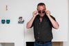 TV-værten Peter Ingemann synes selv, at han ser afvæbnende “sjovt white trash“ ud på fotoet her, der er taget hjemme i privaten ved Silkeborg. På reolen bag ham står en Hitler-sparebøsse fra 1938. Når man lægger en mønt i hånden på Hitler og trykker på ryggen, ryger mønten ind i munden. Sparebøssen er en foræring til den Anden Verdenskrig-interesserede tv-vært fra en antikvitetshandler i Nordsjælland. Foto: Joachim Ladefoged