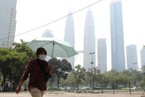 Indbyggere i Kuala Lumpur har iført sig masker for at beskytte sig mod røgen. I baggrunden Twin Towers, der er indhyllet i røgen. Foto: Lim Huey Teng/Reuters
  