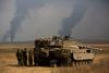 Israelske soldater står ved en kampvogn og betragter røgsøjler stige op over Gazastriben.